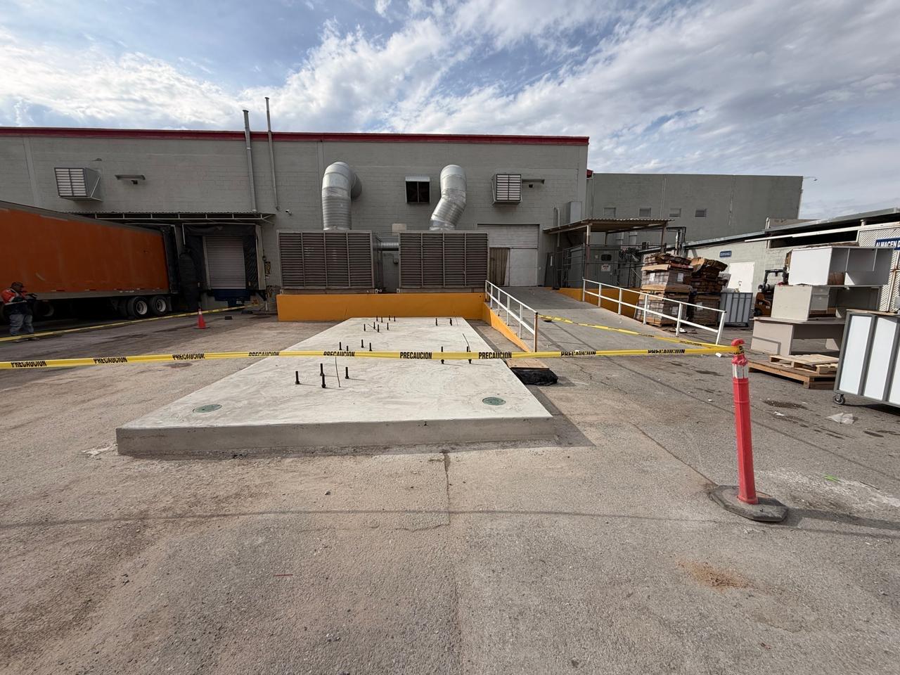 The finished reinforced concrete slab with exposed anchor bolts, cordoned off with caution tape beside an active loading dock